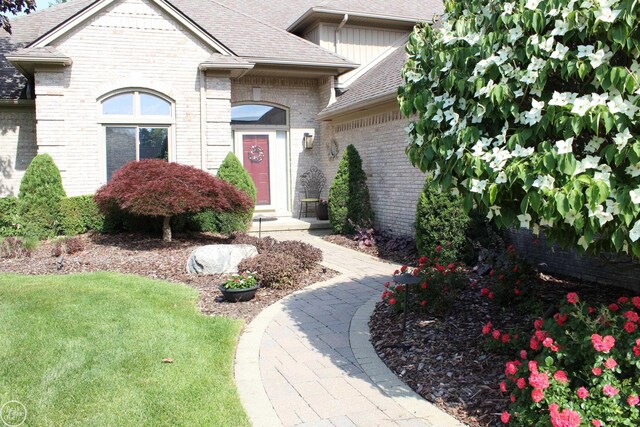 54640 Burlington Dr, Shelby Twp, MI 48315 - view of exterior entry with brick siding, roof with shingles, and a yard