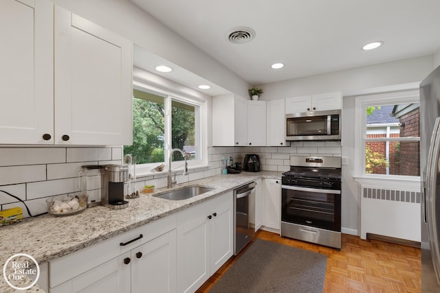 1033 Cadieux Rd, Grosse Pointe, MI 48230 - kitchen with appliances with stainless steel finishes, radiator, decorative backsplash, white cabinetry, and recessed lighting
