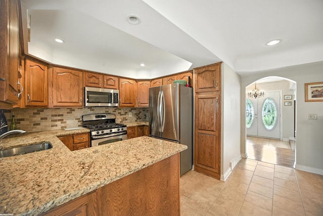 5350 Fieldcrest Dr, Shelby Twp, MI 48316 - kitchen featuring appliances with stainless steel finishes, light stone counters, arched walkways, decorative backsplash, and brown cabinets