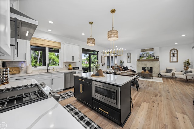 54877 Camden Ct, Shelby Twp, MI 48316 - kitchen with stainless steel appliances, light countertops, white cabinets, range hood, and light wood-type flooring