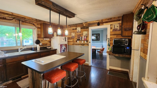 4467 Kings Corner Rd, Glennie, MI 48737 - kitchen with freestanding refrigerator, black microwave, dark countertops, wooden walls, and dark wood-style flooring