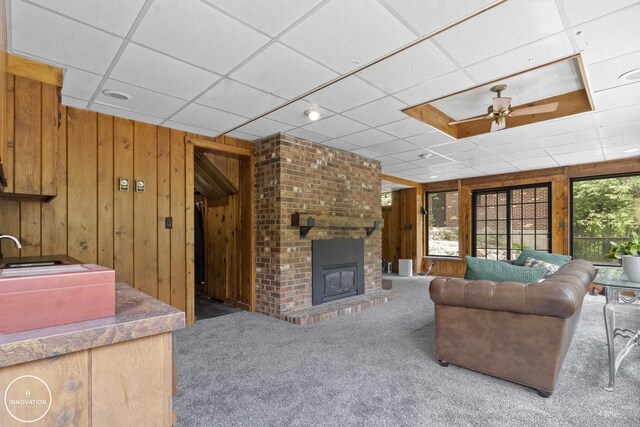 35727 Elm St, Wayne, MI 48184 - living room featuring carpet flooring, wood walls, a drop ceiling, a ceiling fan, and a fireplace