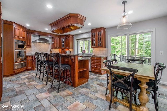 25986 Glenmoor St, Novi, MI 48374 - kitchen featuring a warming drawer, wall chimney range hood, appliances with stainless steel finishes, brown cabinetry, and recessed lighting