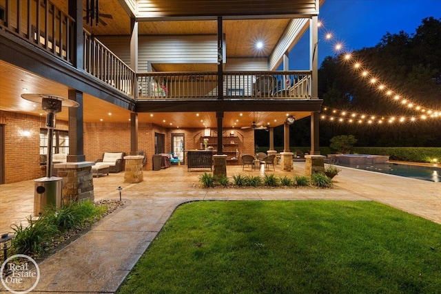 2940 Buell Rd, Oakland Twp, MI 48363 - back of house at night featuring a balcony, a patio, an outdoor pool, a yard, and brick siding