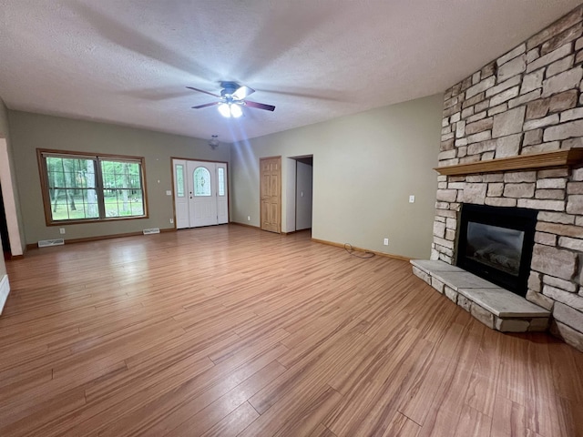876 N Sanford Ln, Au Gres, MI 48703 - unfurnished living room with a fireplace, light wood-style flooring, a ceiling fan, and a textured ceiling