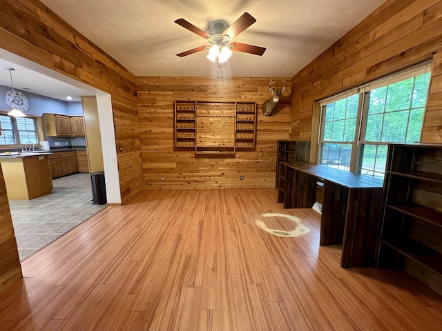 876 N Sanford Ln, Au Gres, MI 48703 - unfurnished living room with wooden walls, ceiling fan, light wood-style floors, and a textured ceiling