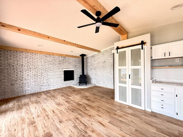 3331 Lakeshore Dr, Gladwin, MI 48624 - unfurnished living room with brick wall, a wood stove, light wood-type flooring, ceiling fan, and a barn door
