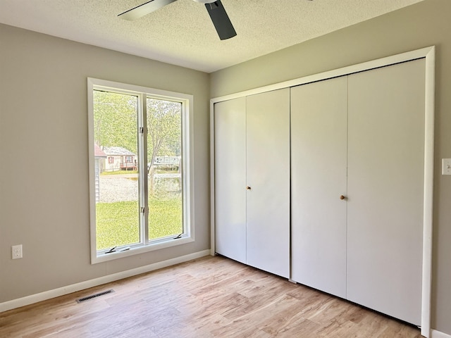 3331 Lakeshore Dr, Gladwin, MI 48624 - unfurnished bedroom with light wood-type flooring, multiple windows, a closet, a textured ceiling, and ceiling fan