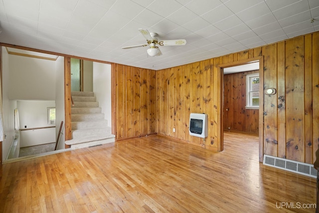 719 S Carlshend Rd, Skandia, MI 49885 - unfurnished living room with heating unit, wood finished floors, wooden walls, ceiling fan, and stairway