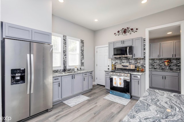 2513 Concord St, Detroit, MI 48207 - kitchen featuring stainless steel appliances, gray cabinetry, backsplash, light wood finished floors, and light stone counters