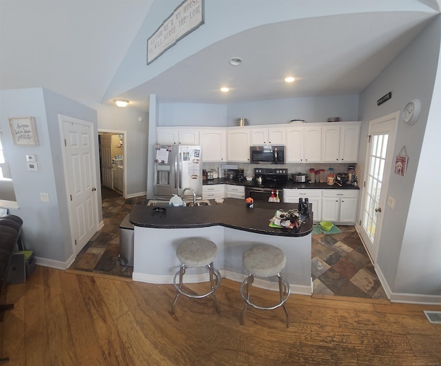 11639 State Rd, Nunica, MI 49448 - kitchen featuring appliances with stainless steel finishes, dark countertops, white cabinetry, vaulted ceiling, and tasteful backsplash