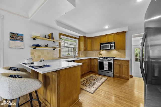 1344 Torrey Rd, Grosse Pointe Woods, MI 48236 - kitchen with stainless steel appliances, a peninsula, light wood-style flooring, brown cabinetry, and tasteful backsplash