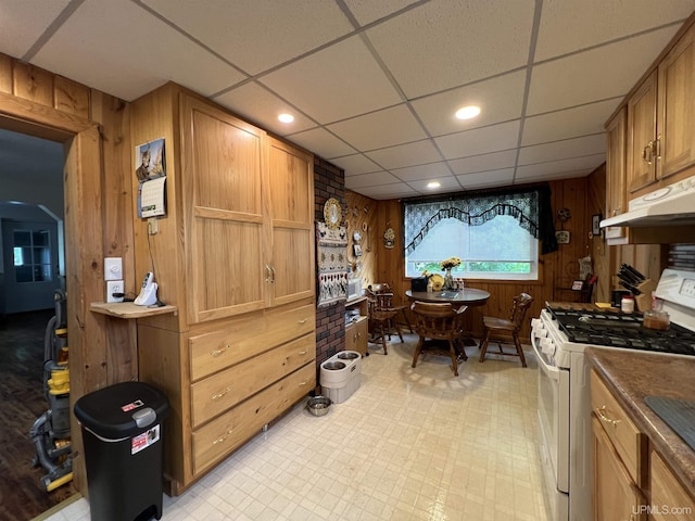 608 W Onota St, Munising, MI 49862 - kitchen featuring white range with gas cooktop, wood walls, under cabinet range hood, light floors, and a drop ceiling