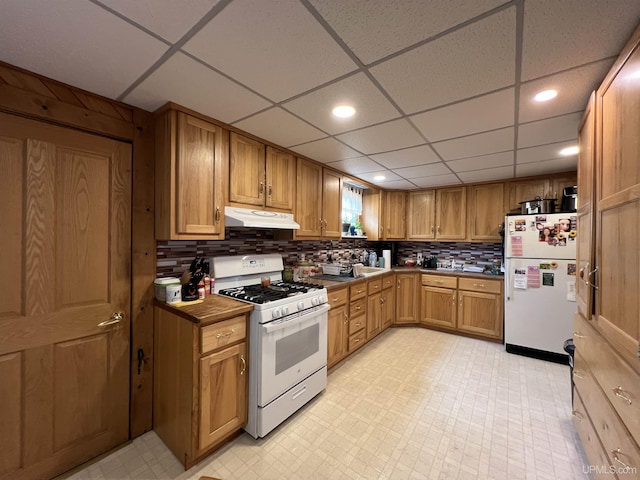 608 W Onota St, Munising, MI 49862 - kitchen featuring white appliances, under cabinet range hood, dark countertops, decorative backsplash, and brown cabinets