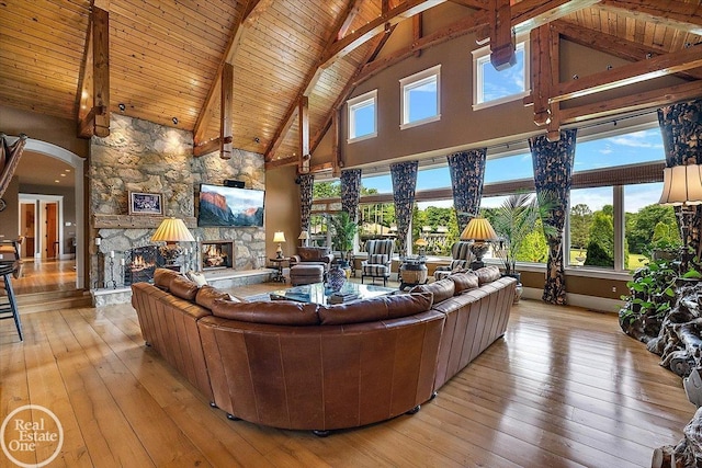 5350 Brewster Rd, Oakland Twp, MI 48306 - living room featuring a stone fireplace, high vaulted ceiling, wood-type flooring, a wooden ceiling with exposed beams, and arched walkways