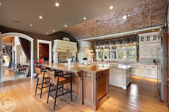 5350 Brewster Rd, Oakland Twp, MI 48306 - kitchen featuring arched walkways, a spacious island, light wood-style flooring, a kitchen bar, and lofted ceiling