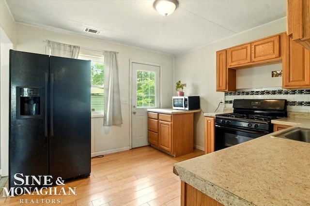 3032 24th St, Port Huron, MI 48060 - kitchen with black appliances, light wood finished floors, light countertops, tasteful backsplash, and brown cabinets