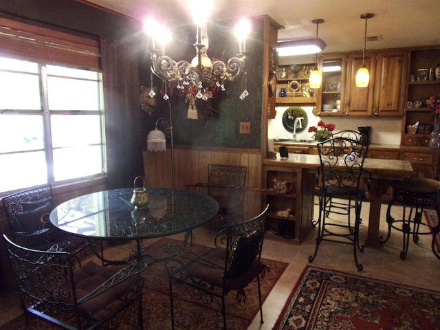 dining space with wood walls, sink, light tile patterned floors, and a notable chandelier