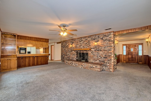 unfurnished living room with wood walls, ceiling fan, light carpet, and a brick fireplace