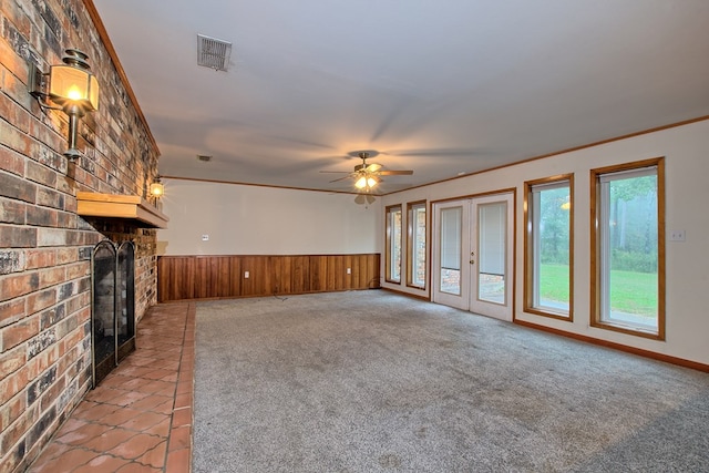 unfurnished living room with wooden walls, a brick fireplace, ceiling fan, ornamental molding, and light colored carpet