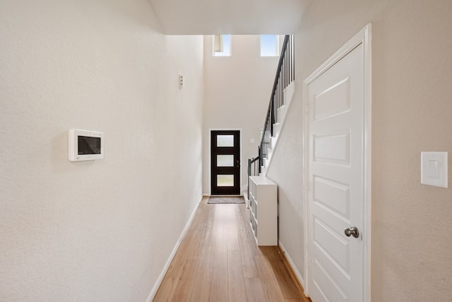 entryway featuring a towering ceiling, baseboards, a wealth of natural light, and light wood-style floors
