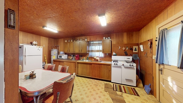 kitchen featuring white appliances, electric water heater, kitchen peninsula, wooden walls, and sink