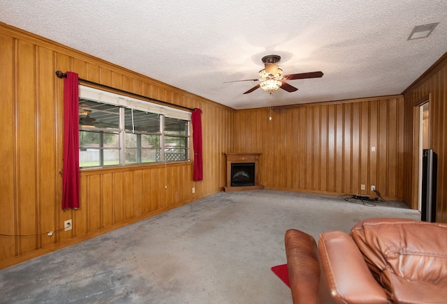 carpeted living room with ceiling fan, ornamental molding, a textured ceiling, and wooden walls