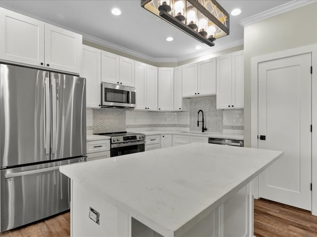 kitchen featuring wood finished floors, appliances with stainless steel finishes, ornamental molding, and a sink