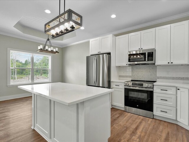 kitchen featuring a center island, wood finished floors, appliances with stainless steel finishes, backsplash, and ornamental molding
