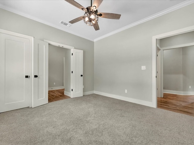 unfurnished bedroom featuring baseboards, visible vents, ceiling fan, carpet floors, and ornamental molding