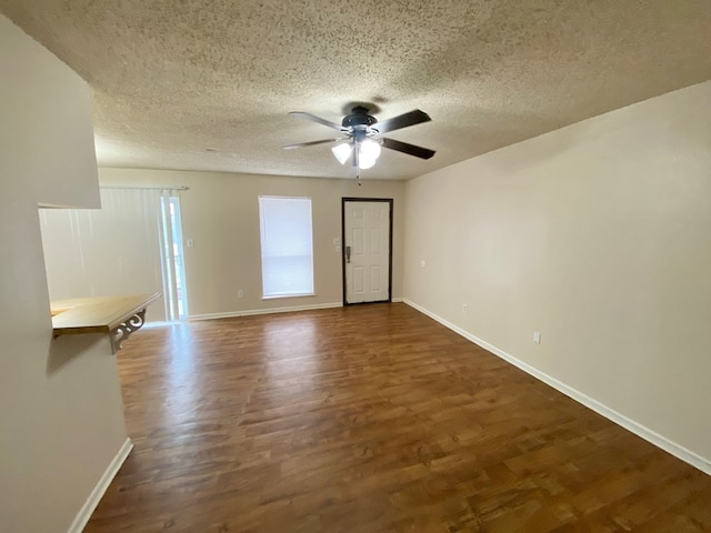 empty room with a textured ceiling, ceiling fan, and dark hardwood / wood-style floors