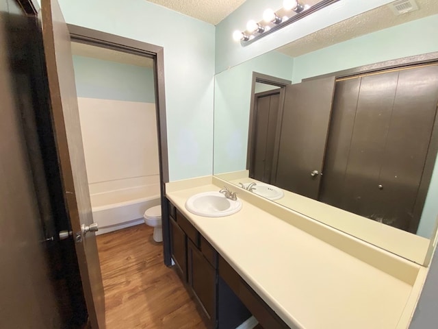 full bathroom featuring shower / bathtub combination, vanity, a textured ceiling, hardwood / wood-style flooring, and toilet