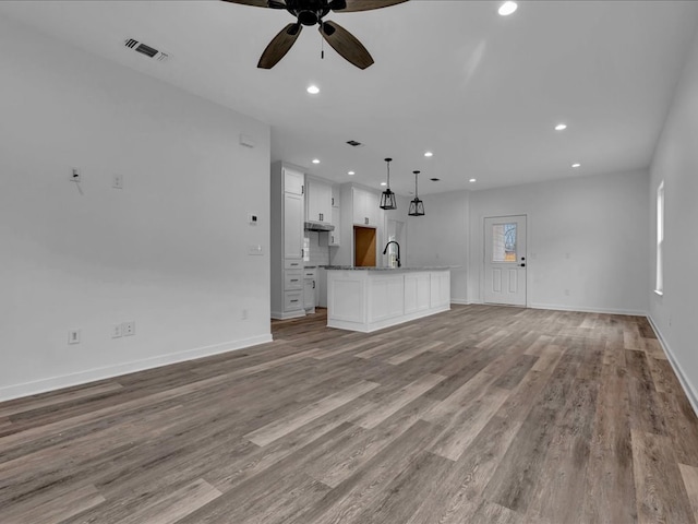 unfurnished living room with ceiling fan, a healthy amount of sunlight, sink, and light hardwood / wood-style flooring