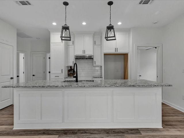 kitchen with pendant lighting, light stone countertops, an island with sink, and white cabinets