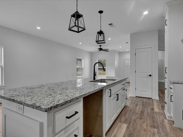 kitchen featuring sink, white cabinetry, light stone counters, hanging light fixtures, and a kitchen island with sink