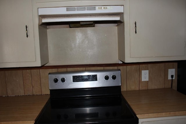 kitchen with electric stove, white cabinets, and under cabinet range hood