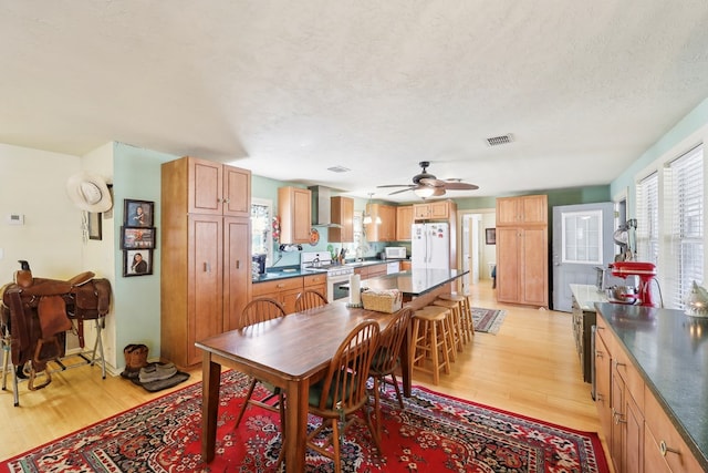 dining space featuring a ceiling fan, visible vents, a textured ceiling, and light wood finished floors