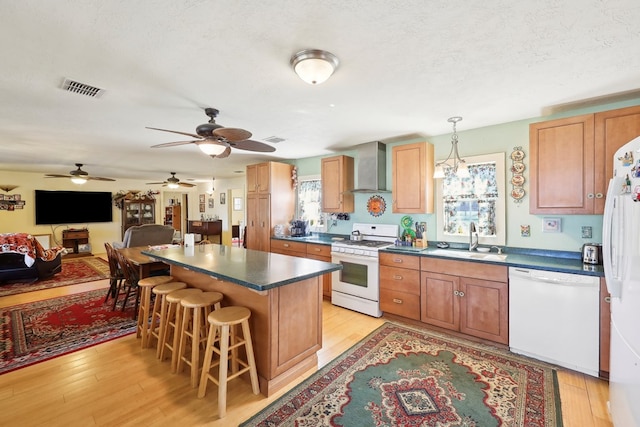 kitchen featuring dark countertops, light wood-style floors, a sink, wall chimney range hood, and white appliances