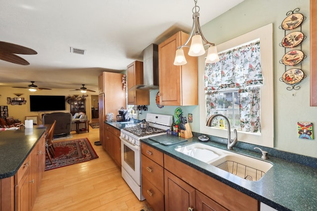 kitchen featuring light wood finished floors, visible vents, a sink, wall chimney range hood, and white range with gas stovetop