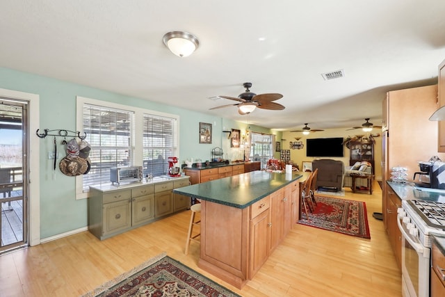 kitchen with white range with gas stovetop, visible vents, light wood-style flooring, a kitchen island, and a breakfast bar area