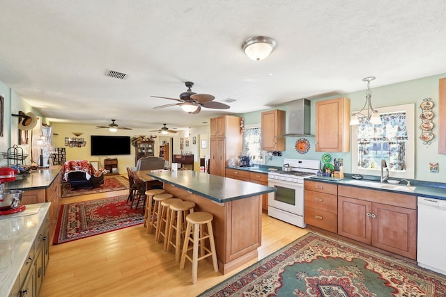 kitchen with light wood finished floors, visible vents, a sink, wall chimney range hood, and white appliances