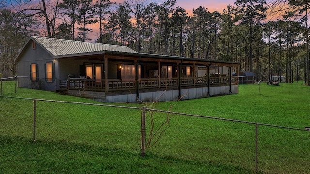 rear view of house featuring metal roof, a lawn, and fence