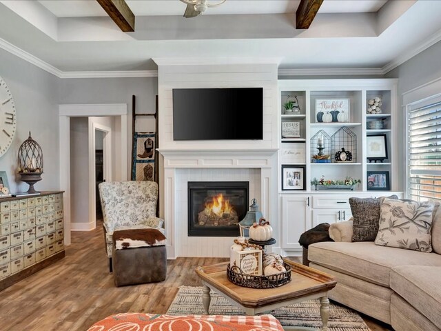 living room featuring a large fireplace, beamed ceiling, ornamental molding, and light wood-type flooring