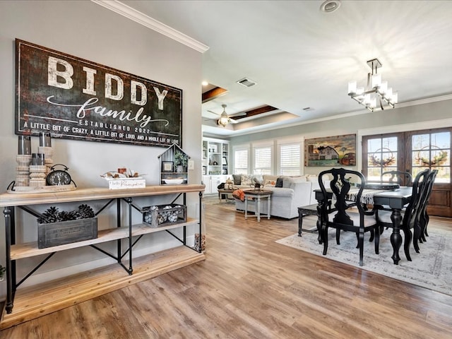 dining space with wood-type flooring, ceiling fan with notable chandelier, a raised ceiling, and ornamental molding