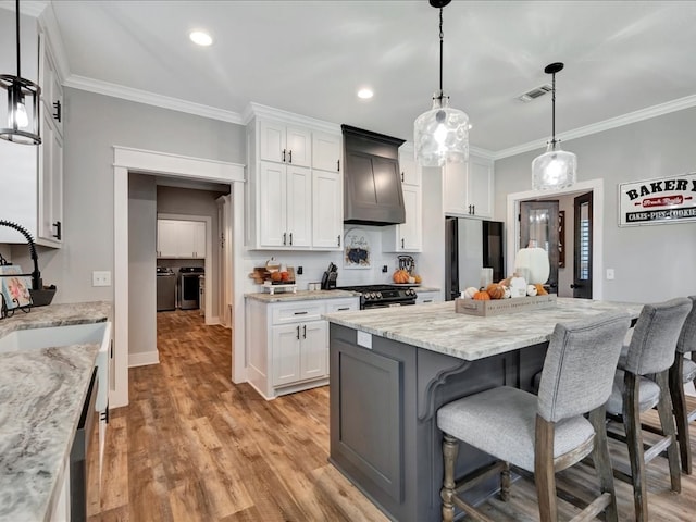 kitchen featuring custom exhaust hood, sink, hanging light fixtures, appliances with stainless steel finishes, and white cabinetry