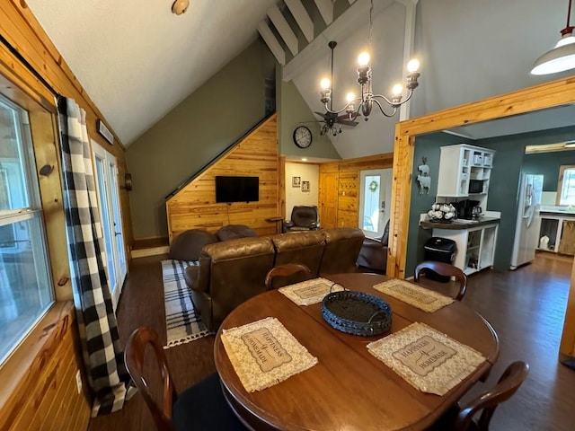 dining area with wooden walls, high vaulted ceiling, an inviting chandelier, and wood finished floors