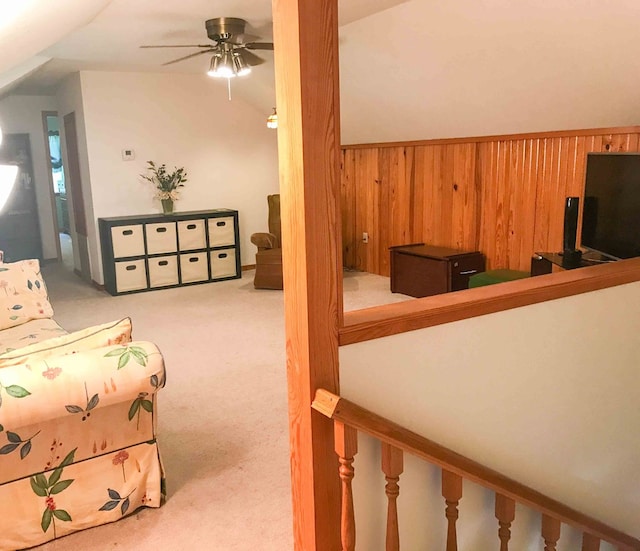 carpeted living room with ceiling fan, wooden walls, and vaulted ceiling