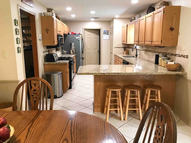 kitchen with kitchen peninsula, light stone countertops, stainless steel appliances, sink, and a breakfast bar area