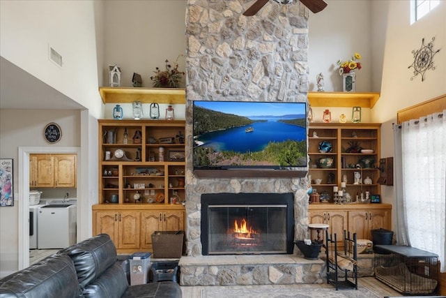 living room featuring washer and dryer, ceiling fan, a stone fireplace, and a towering ceiling