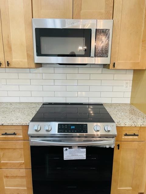 kitchen with backsplash, light stone counters, light brown cabinets, and stainless steel appliances